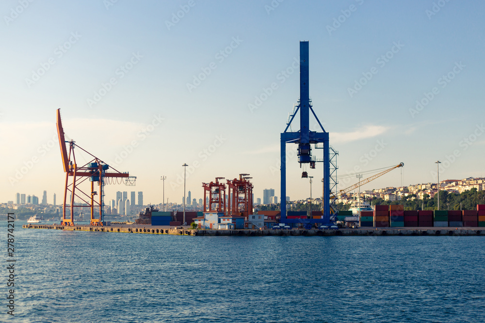 Fototapeta premium Cranes and Containers at container freight station of Haydarpasa Port. View from sea in daytime and city scape on the back.