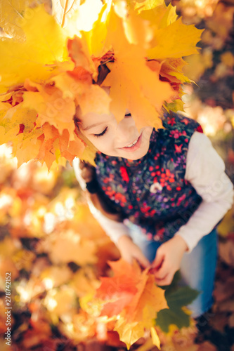 Portrait of smiling child with wreath of leaves on head and a bouquet of leaves in the hands. Background of sunny autumn park.