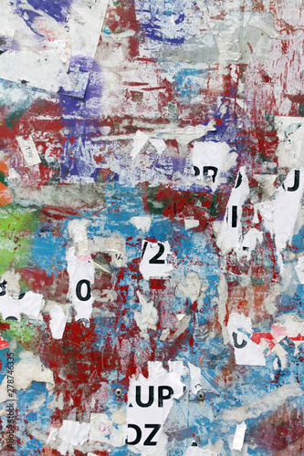 Grungy flat wall surface covered with pealed paper and red, green and blue spray paint 