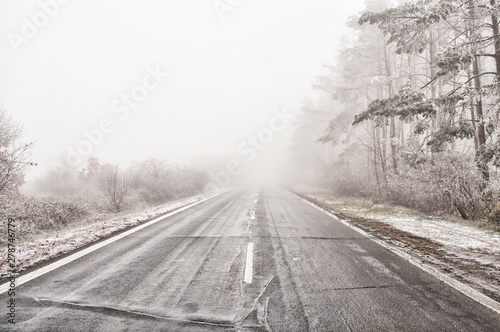 Straight empty wet asphalt road during foggy conditions