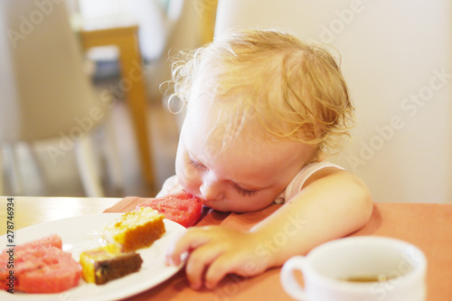 A small child sits at a table in a Turkish restaurant and sleeps. The child ate watermelon.