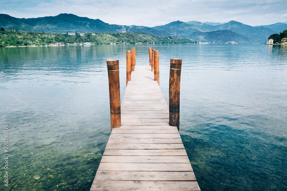 Naklejka premium Wooden pier on Orta San Giulio Lake with greenery mountain background. Italy.