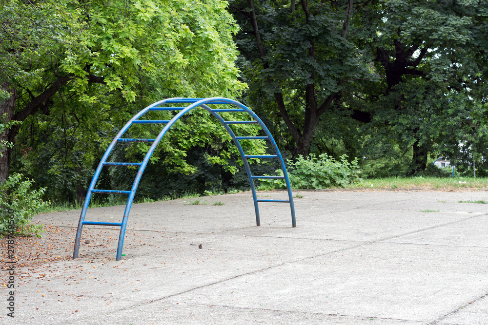 Blue climbing ladder on a concrete children's playground, in front of green park trees Blue climbing ladder on a concrete children's playground, in front of green park trees