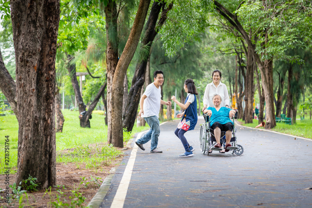 Happy family,asian child girl or daughter playing touch,tag game,run with father,elderly woman in wheelchair in outdoor park,mother,senior grandmother having fun,laugh,parents enjoy vacation concept
