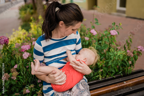 young brunete mother breast feeding baby girl outdoors in public town  photo