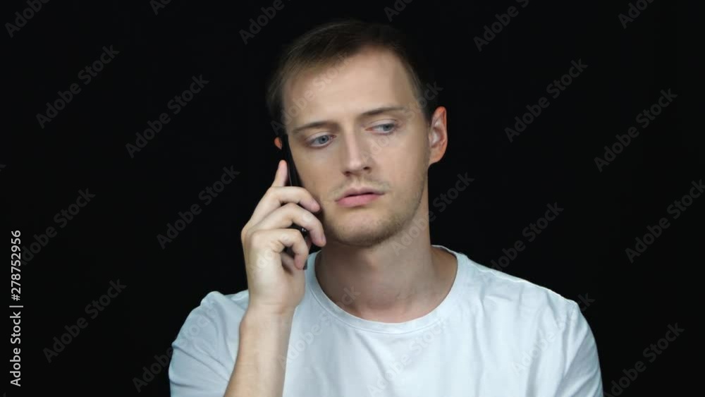 Young man irritated and tired while speaking on a mobile phone at black backround. Portrait. Young man irritated and tired while speaking on a mobile phone at black backround. Portrait.