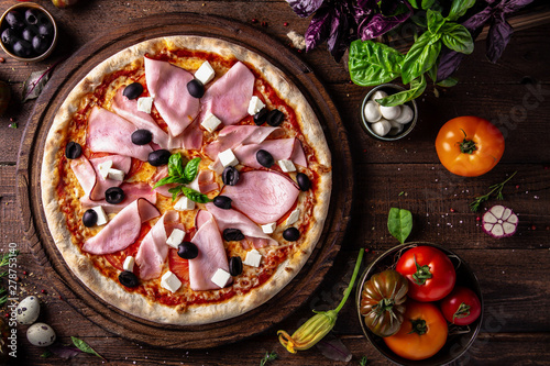 Tasty hot italian pizza Queen with Bacon, Baked Pork, Tomatoes, Olives, Cheese, Feta, Mozzarella, Basil and Sauce on old wooden table. Pizzeria menu. Concept poster for Restaurants or pizze photo