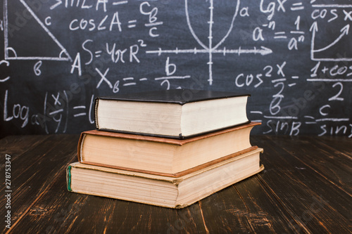 Books on a wooden table, against the background of a chalk board with formulas. Teacher's day concept and back to school.