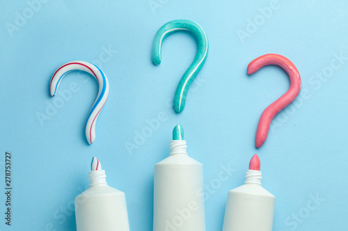 Question mark from toothpaste. Concept of choosing good toothpaste for teeth whitening. Tube of colored toothpaste on blue background. Copy space for text.