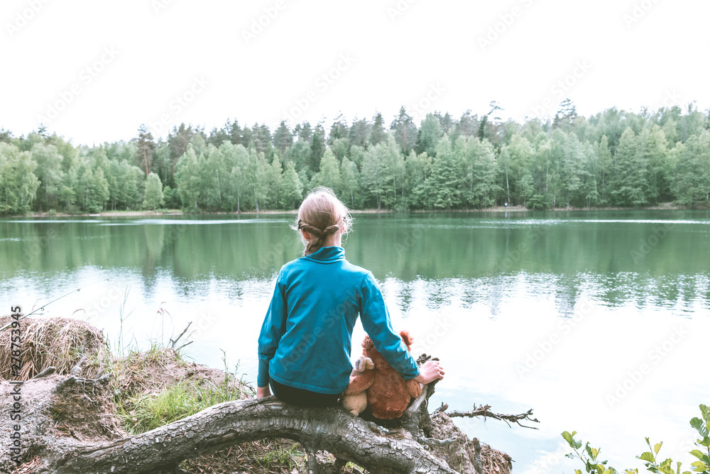 Cute Caucasian little girl on the lake with her plush toys, teddy bear and bunny. Back view, Cute Caucasian little girl on the lake with her plush toys, teddy bear and bunny. Back view,