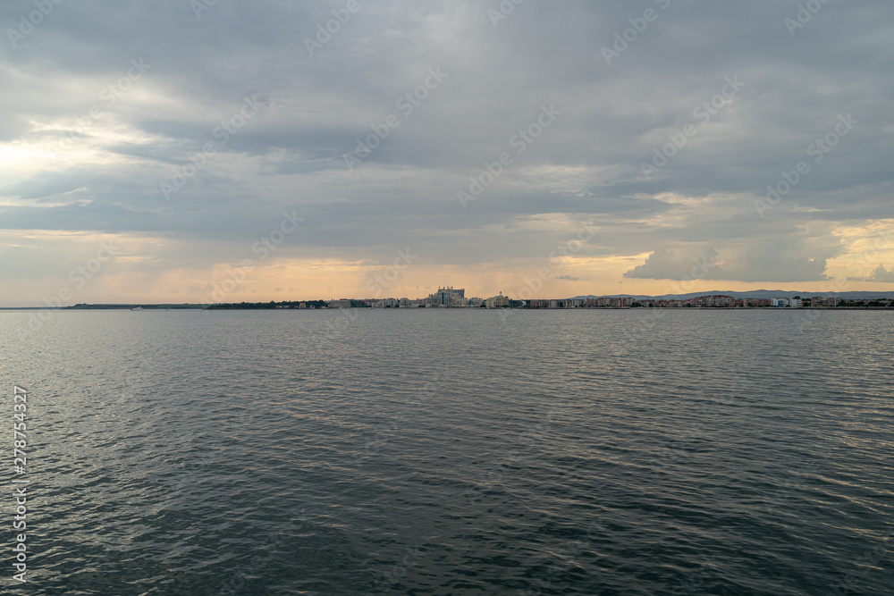 Seascape. Evening overcast sky and the rays of the sun. View on the seaside town of Pomorie. Bulgaria.