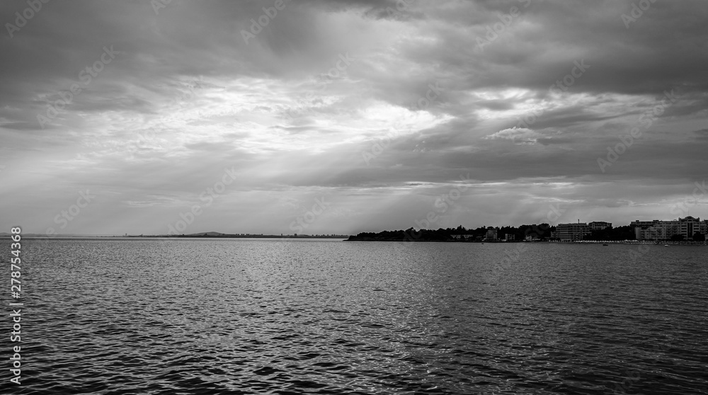 Seascape. Evening overcast sky and the rays of the sun. Black and white.