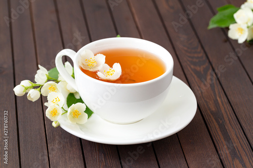 Jasmine tea with jasmine flowers on wooden table background. Cup of hot green tea with jasmine flavor, fresh jasmine flowers. Concept of freshly drink.