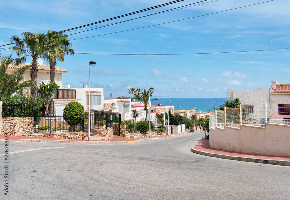 Roadside view to the empty road leading to Mediterranean Sea, coastal summer villas residential houses, blue cloudy sky, picturesque landscape. La Mata, Province of Alicante, Costa Blanca, Spain