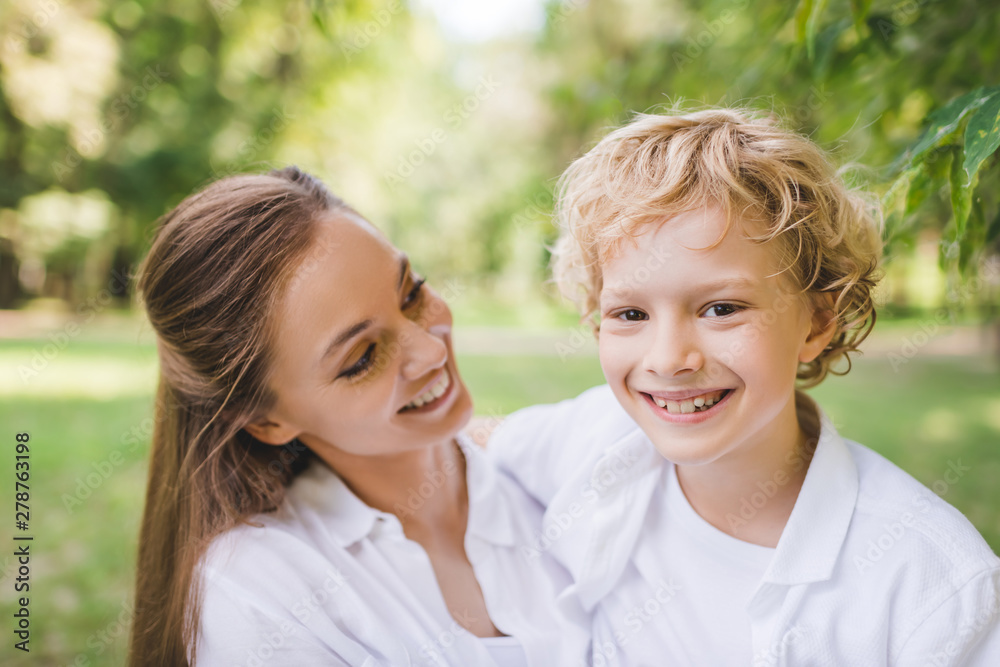 beautiful mother with happy adorable son looking at camera in park beautiful mother with happy adorable son looking at camera in park