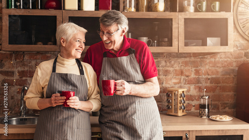 Cheerful seniors drinking morning coffee and talking at kitchen