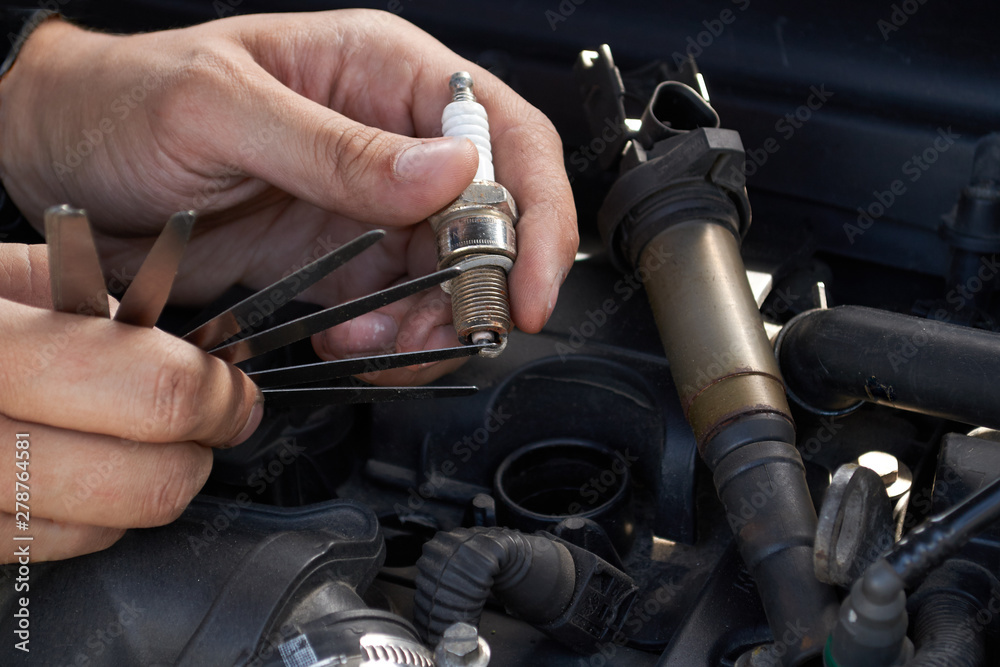 A man checks the spark gap in the spark plug with a probe, close-up