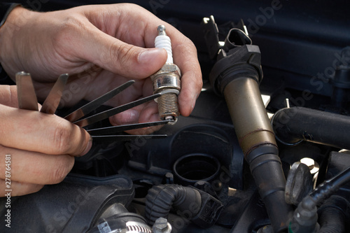 Obraz na płótnie A man checks the spark gap in the spark plug with a probe, close-up w salonie