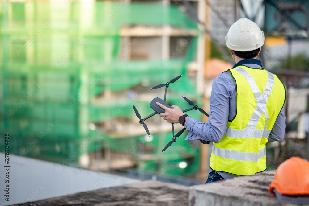 Asian engineer man holding drone at construction site. Male worker using unmanned aerial vehicle (UAV) for land and building site survey in civil engineering project.