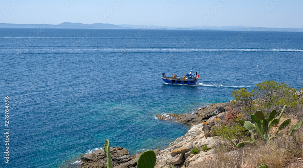 Small fishing boat at the sea. Fishing near the shore in the mediterranean sea. Amazing sunny day, calm blue water. Fishing in the coastal bay. Boat in the sea near the rocks.