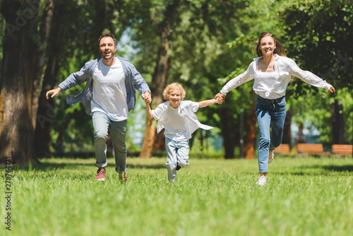 smiling family holding hands and running in park during daytime
