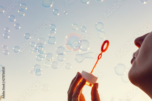 Young woman blowing bubbles to the sky at sunset.