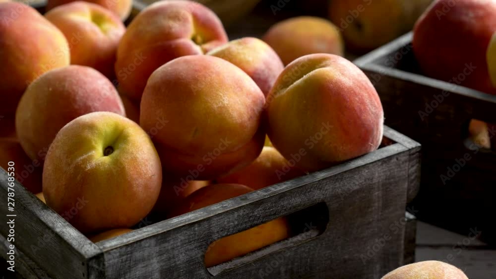 Camera slides to the right showing closeup of fresh peaches in rustic crates on painted wood background with beautiful soft lighting. Camera slides to the right showing closeup of fresh peaches in rustic crates on painted wood background with beautiful soft lighting.