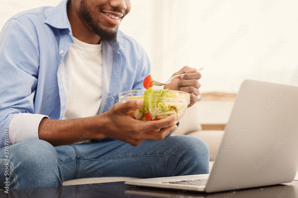 Black man eating vegetable salad at work with laptop Black man eating vegetable salad at work with laptop