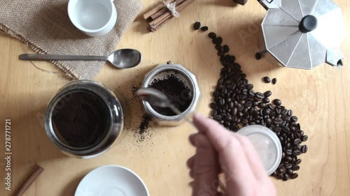Hand holding a spoon preparing some expresso cafe with a coffee pot on a rustic wooden table. Next, some ground coffee and beans with cinnamon. Overhead shot for a top view.
