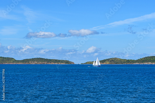 White yacht under a blue sky with clouds on the blue waves of the Caribbean sea against the mountains on the horizon.