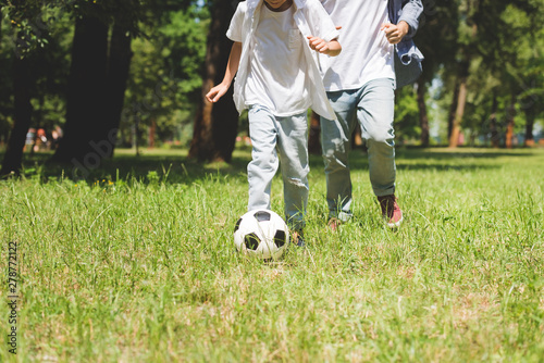 cropped view of father and son playing football with soccer ball in park