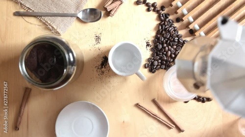 Hand serving some expresso cafe holding a coffee pot on a rustic wooden table. Next, some ground coffee and beans with cinnamon. Slow motion overhead shot for a top view.