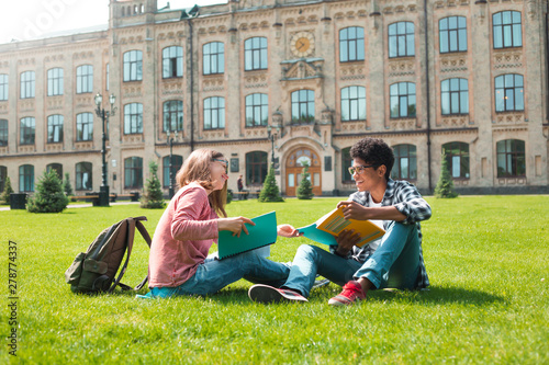 Smiling students African American male in glasses with books and a girl near college. 