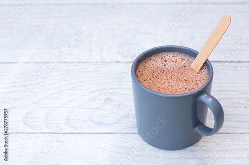 Hot chocolate in a blue-grey ceramic mug with wooden stirrer isolated on white painted wood. Space for text. photo