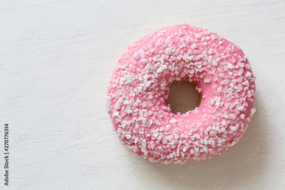 Pink frosted donut sprinkled with crystal sugar isolated on white painted board from above. Space for text. Pink frosted donut sprinkled with crystal sugar isolated on white painted board from above. Space for text.