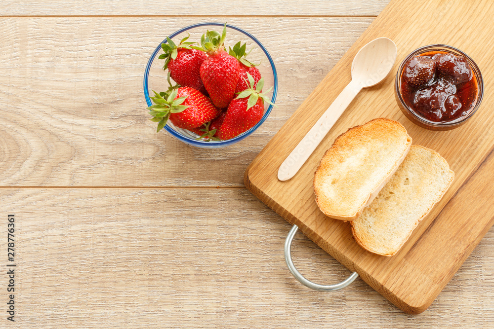 Traditional homemade strawberry jam in bowl, fresh berries with toast on wooden background.