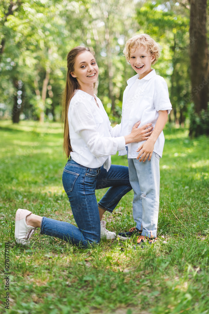 Fototapeta premium beautiful smiling mom hugging son in park and looking at camera
