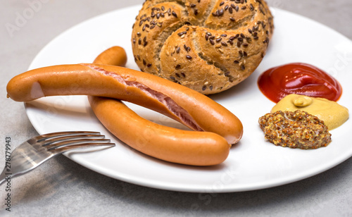 Fresh boiled Vienna sausages or Frankfurter Wurstchen served simply with Kaiser rolls, ketchup and mustard on white plate