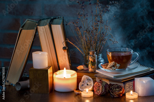 A cup of tea, books, candles, smoke. Mysterious dark still life. Dried flowers. Fairy atmosphere.