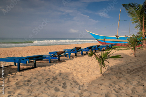 Fischerboot mit blauen Sonnenliegen am Strand von Sri Lanka