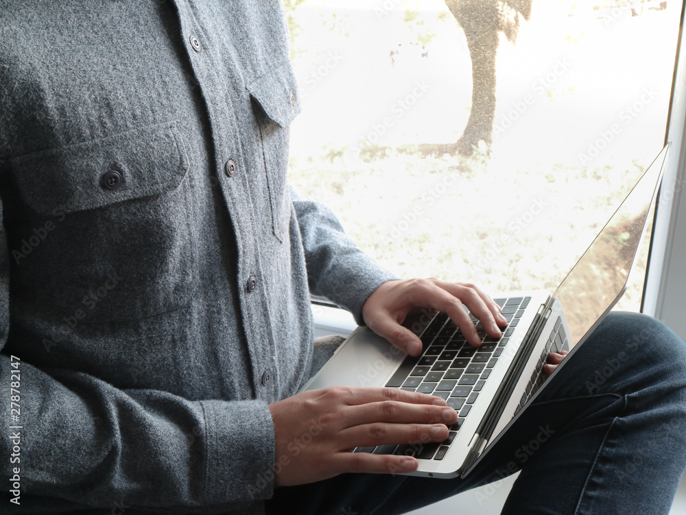 Naklejka premium White businessman typing on a laptop and seated near to a window
