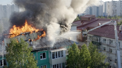 Burning roof of a residential high-rise building, clouds of smoke from the fire. firefighters extinguish the fire. top view