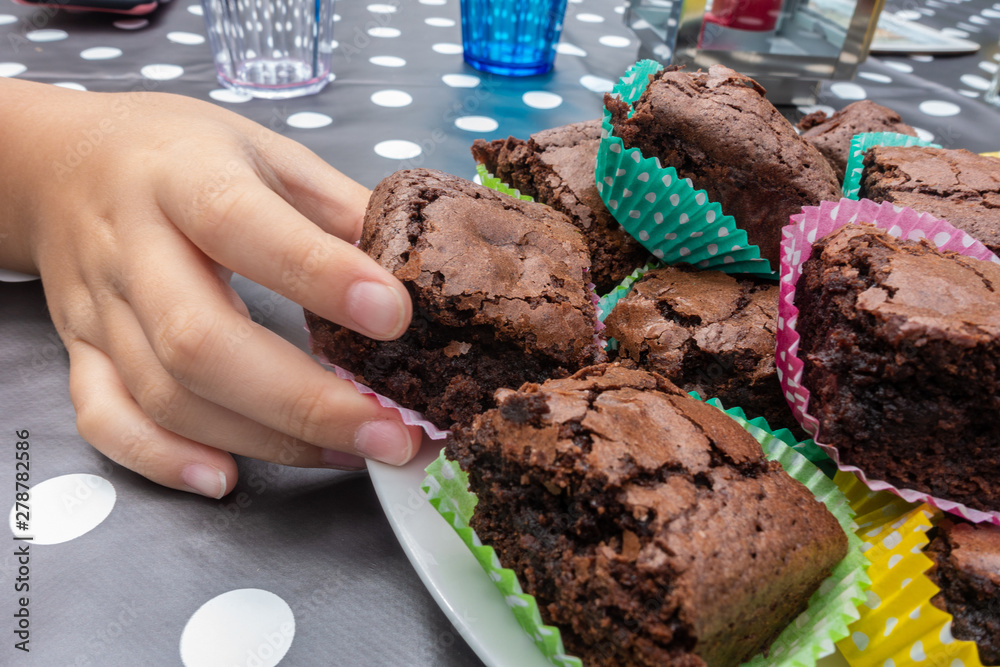 Φωτογραφία A child's hand takes a piece of brownie in a paper case from a plate on a table