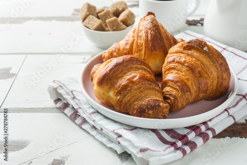 Breakfast croissants on a plate and a Cup of coffee, wooden background, copy space.