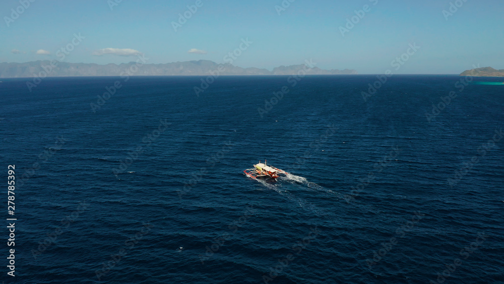 Obraz premium Aerial view tour boat in sea. Seascape blue sea and tropical islands. traditional Filipino wooden outrigger boat called a banca . Motorboat crossing ocean. Banca boat in the Philippines Palawan