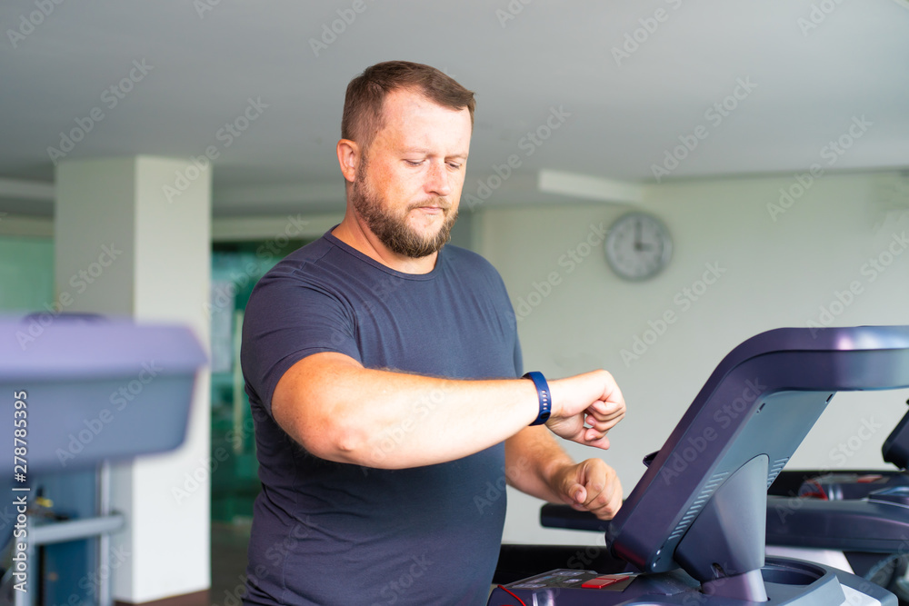full male runs on a treadmill in the gym and looks at the smart watch. concept of weight loss and sport. side view