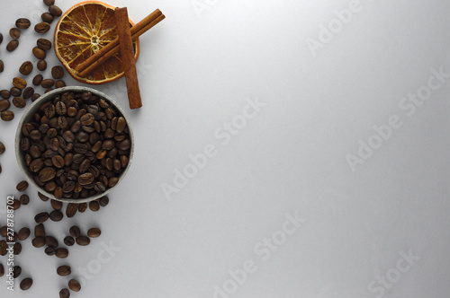 Coffee beans in a concrete bowl on a gray background along with cinnamon sticks and dried orange