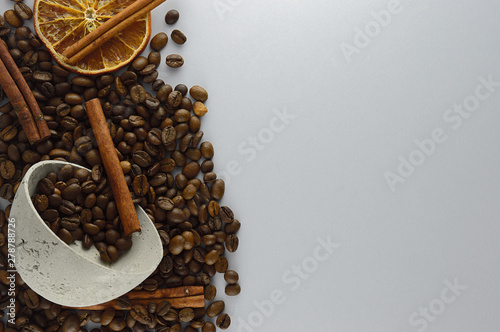 Coffee beans in a concrete bowl on a gray background along with cinnamon sticks and dried orange