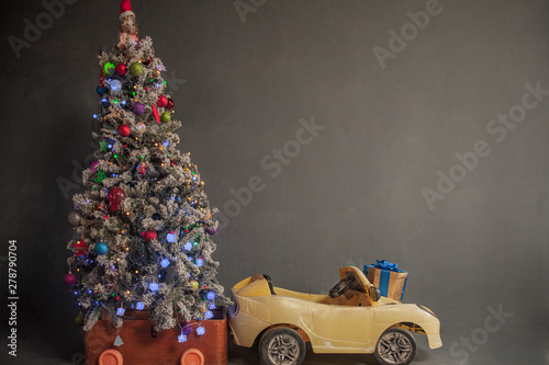 Happy child are dressed in festive costume of Santa Clausn, carrying decorated Christmas tree with balls and garlands on yellow car. Christmas Eve photo