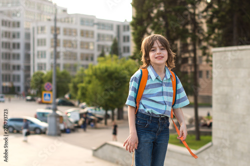 A schoolboy blond, wearing in a shirt and jeans, walks with a knapsack goes by the big ancient building to school.